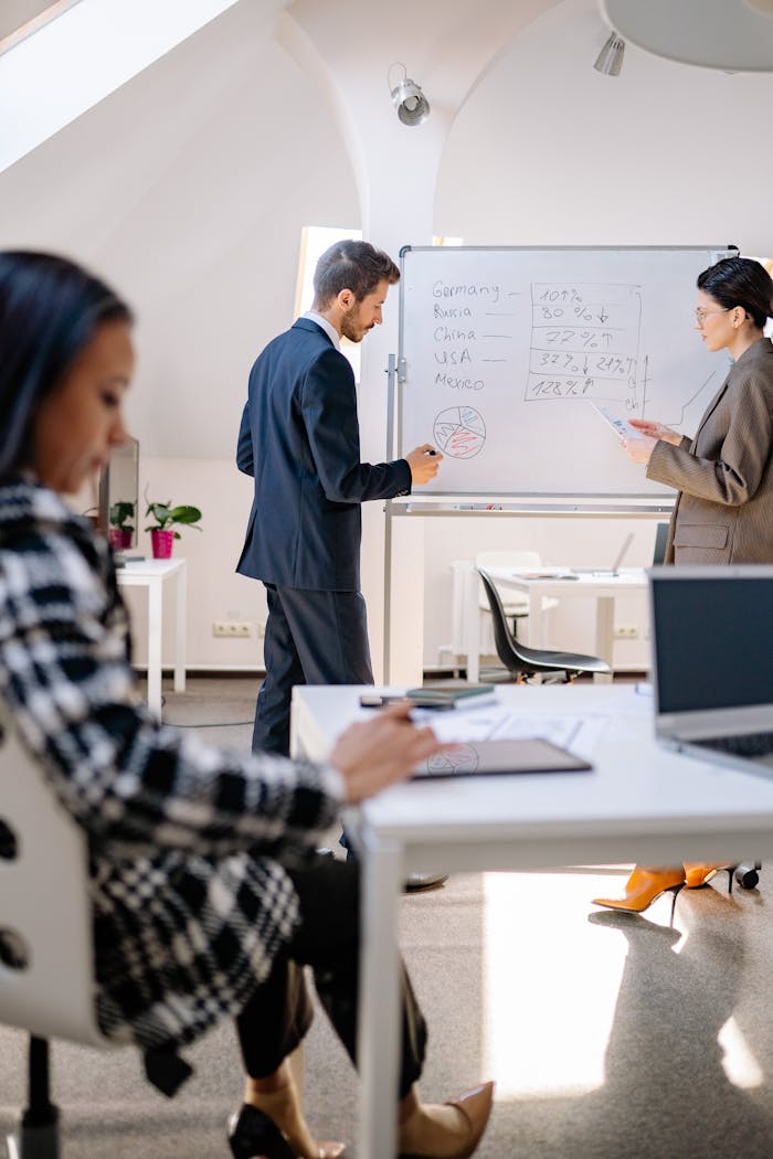 hero-img-02 Business professionals collaborating on data analysis with a whiteboard in a modern office setting.
